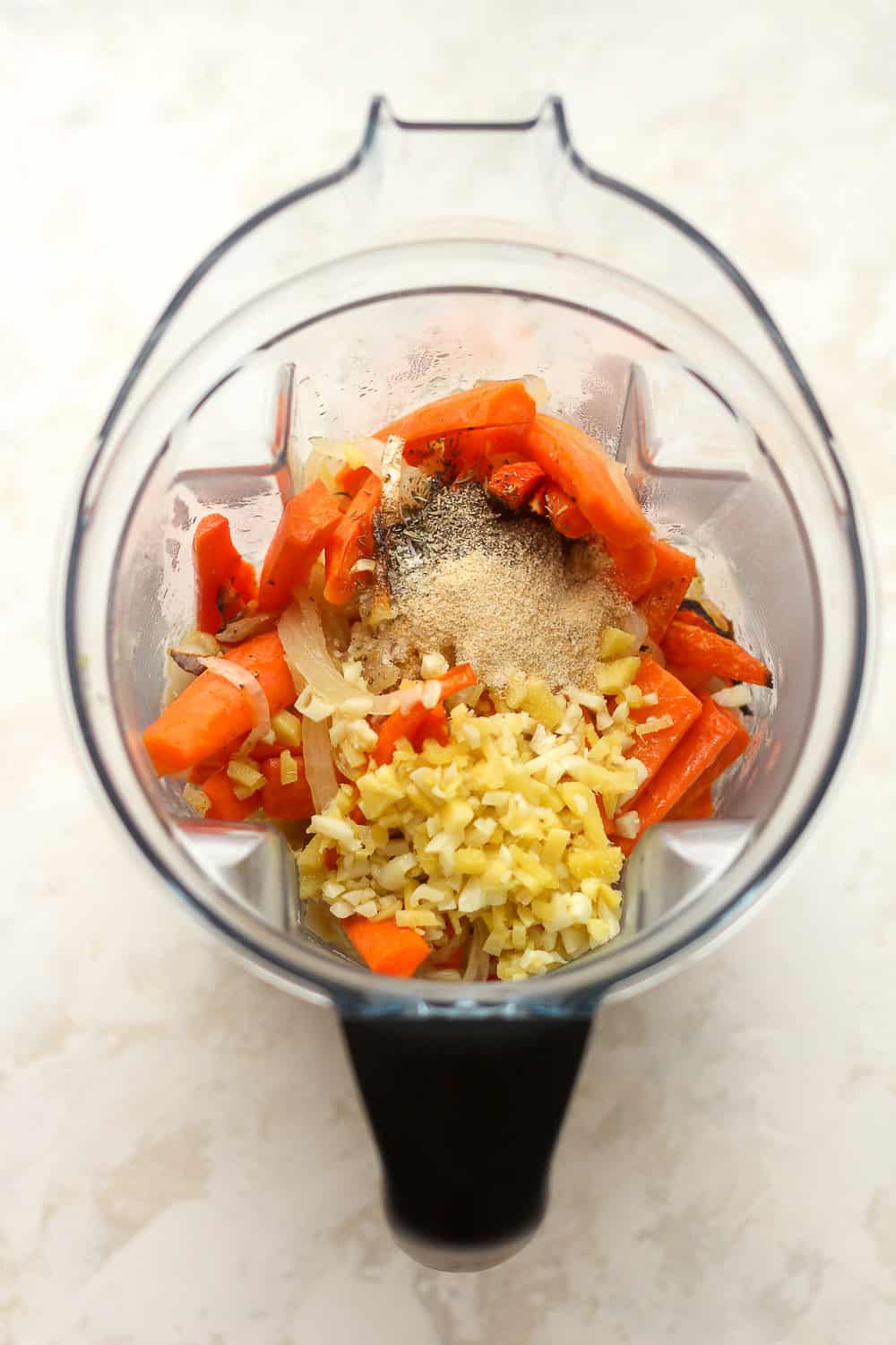 A blender with the roasted carrots plus ginger, garlic, and seasoning on top.