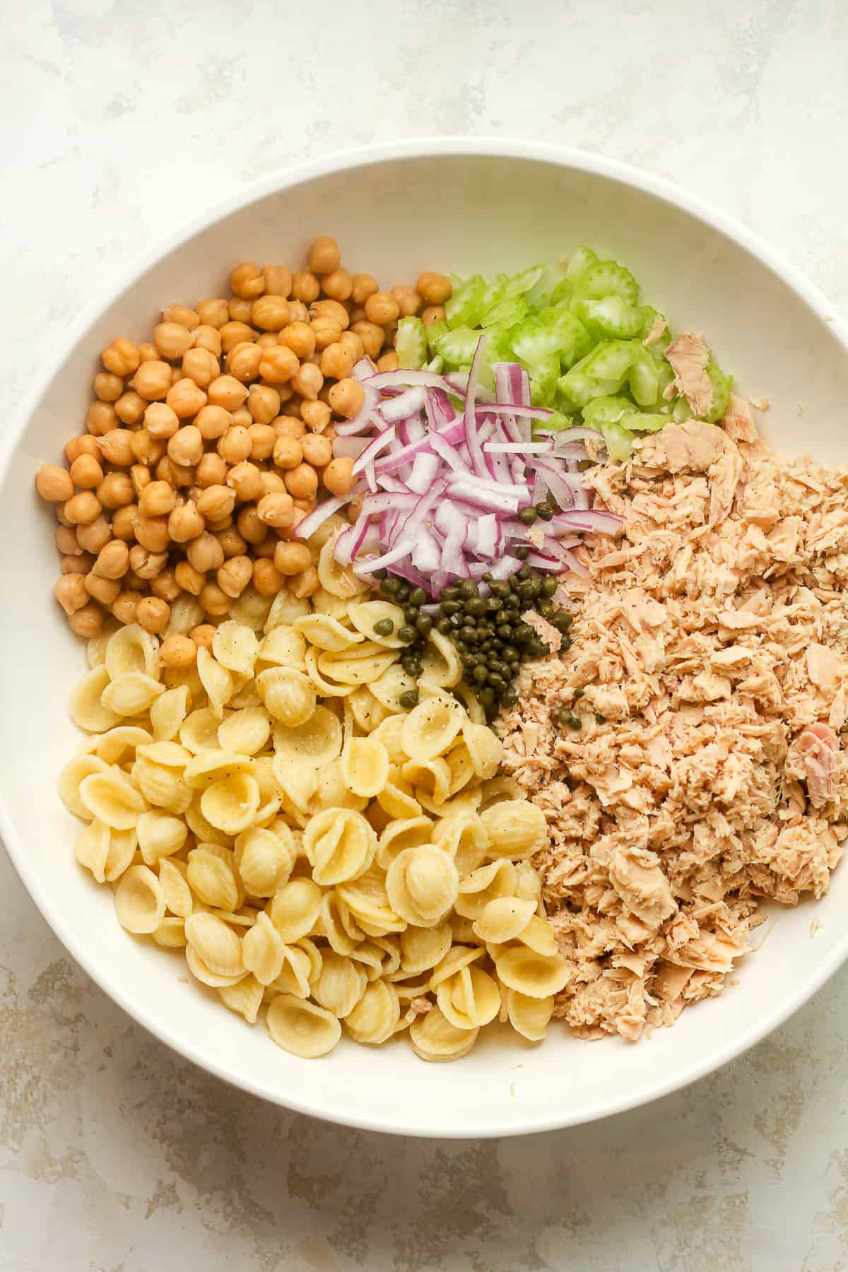 A large bowl of the pasta salad ingredients separated by ingredient.