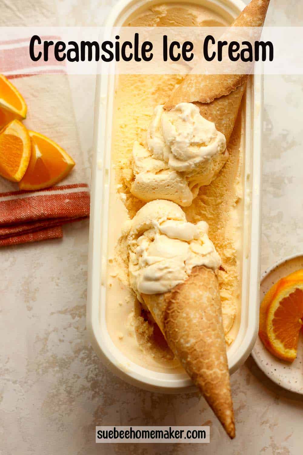 An oblong container of creamsicle ice cream with two ice cream cones inside.