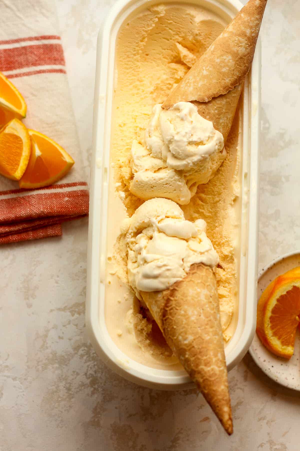 An oblong container of orange ice cream cones inside.