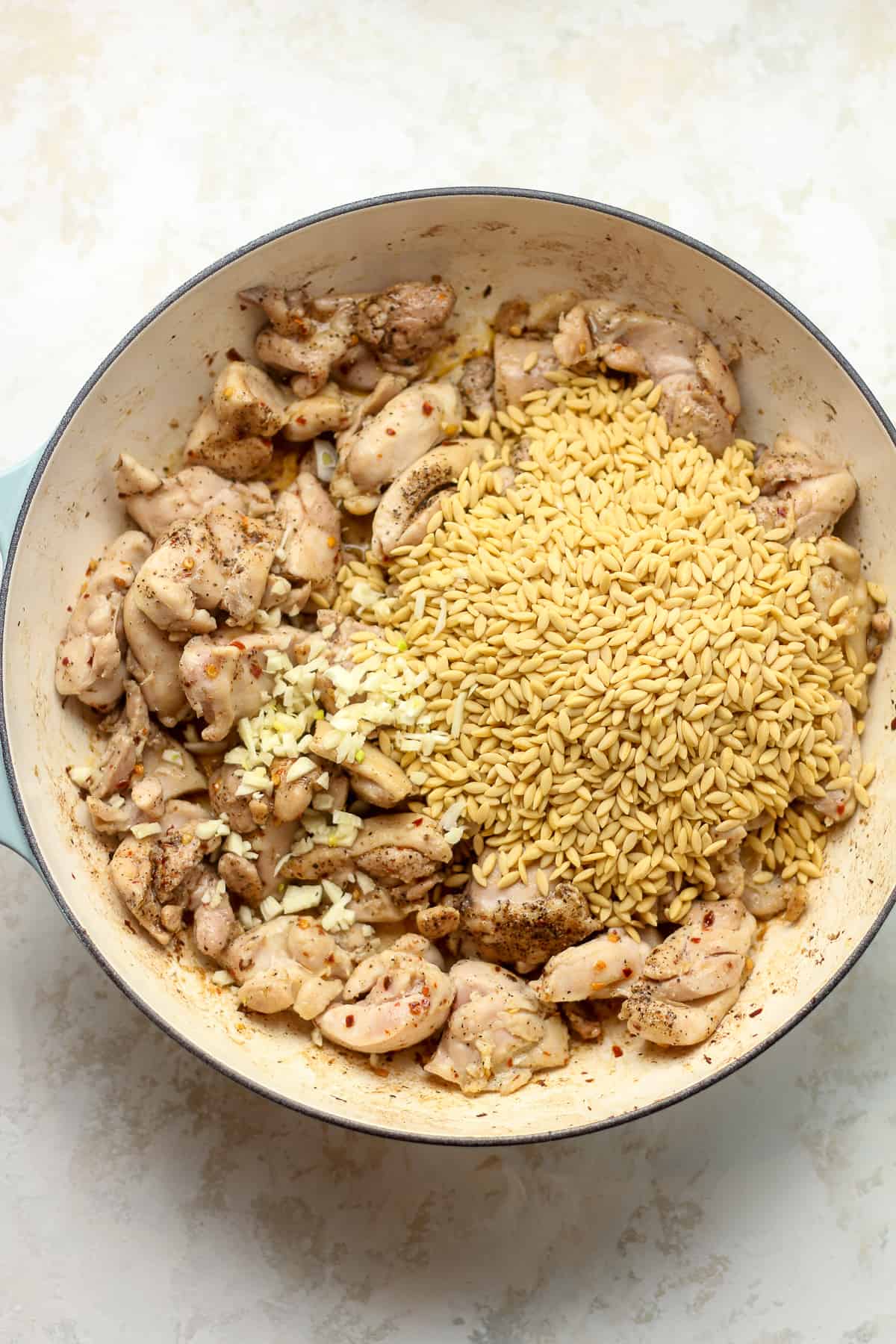 A pot of the browned chicken with orzo and garlic on top.