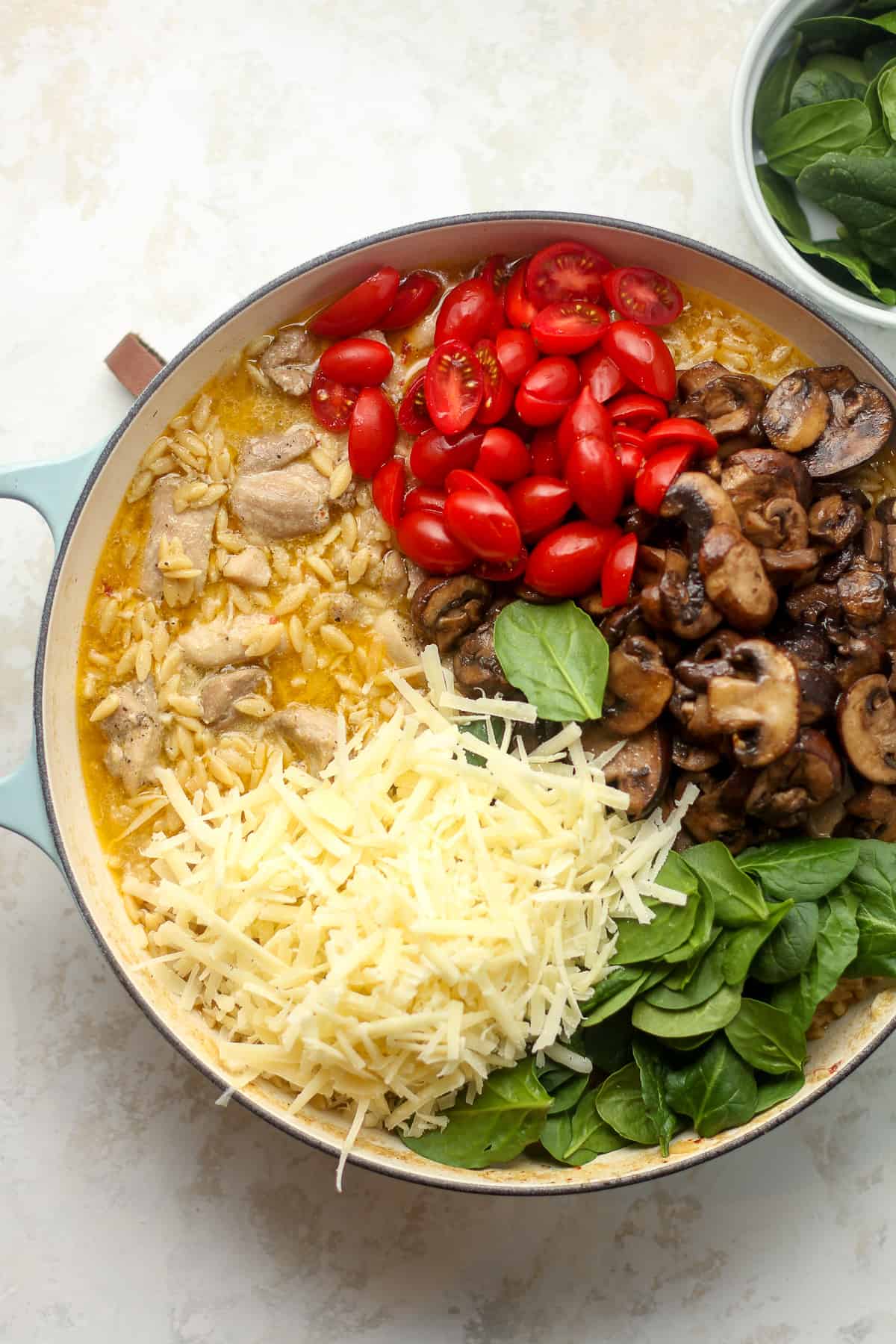 A pot of the cooked chicken and orzo with the tomatoes, mushrooms, spinach, and parmesan on top.