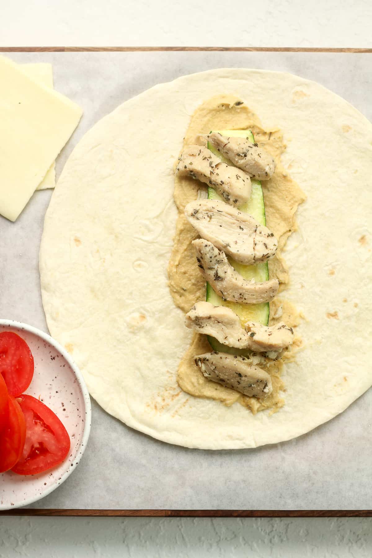 A tortilla with hummus, zucchini, and chicken slices.