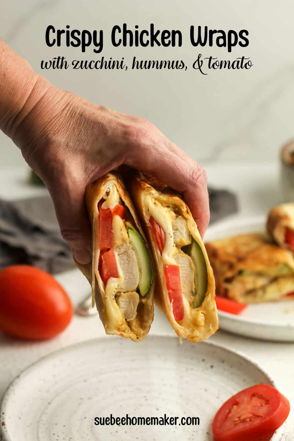 A hand holding a crispy chicken wrap with zucchini and tomato.