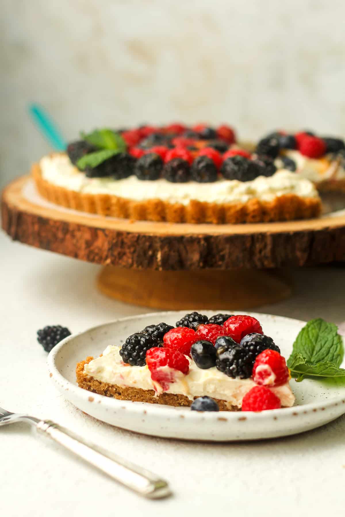Side view of a plate with a slice of fruit tart and the rest in the background.
