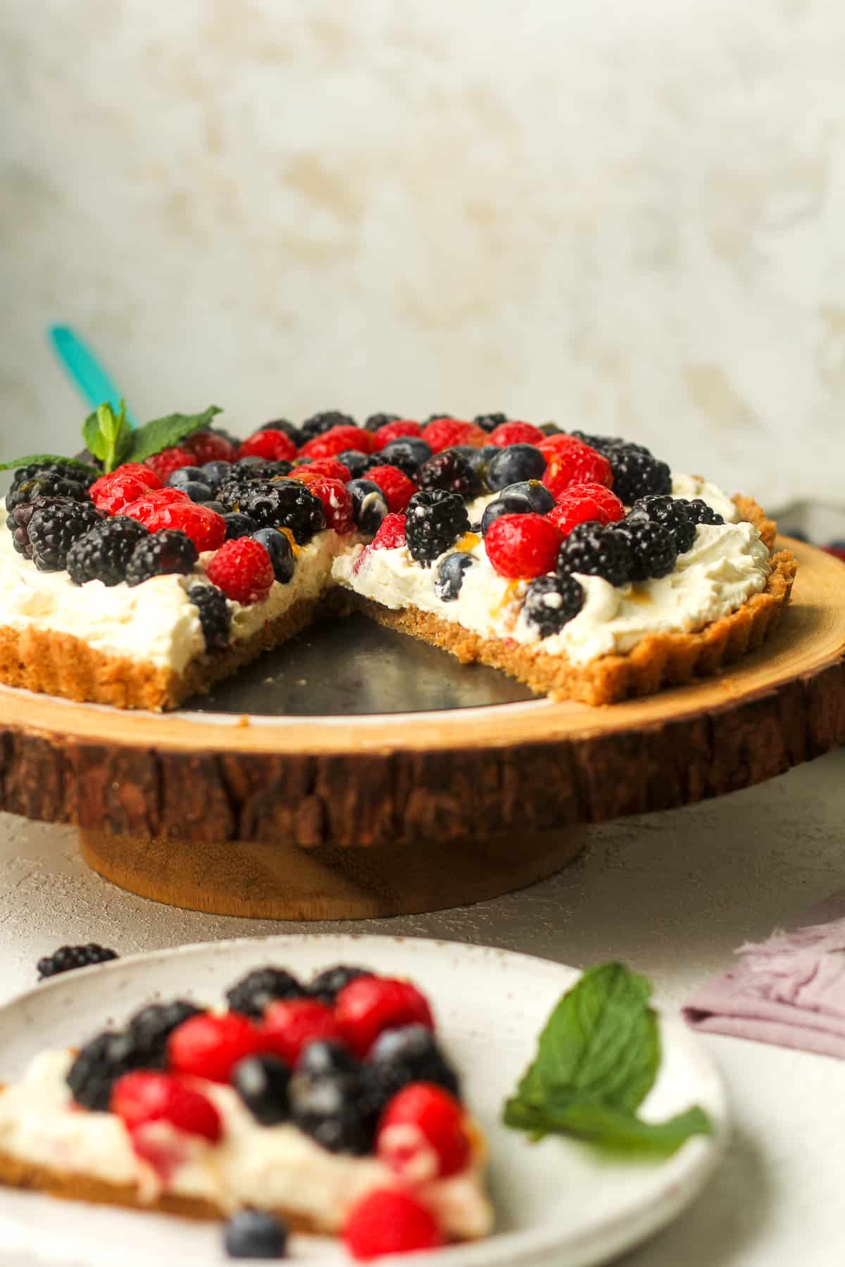 Side view of a cream cheese fruit tart with a slice on a serving plate.