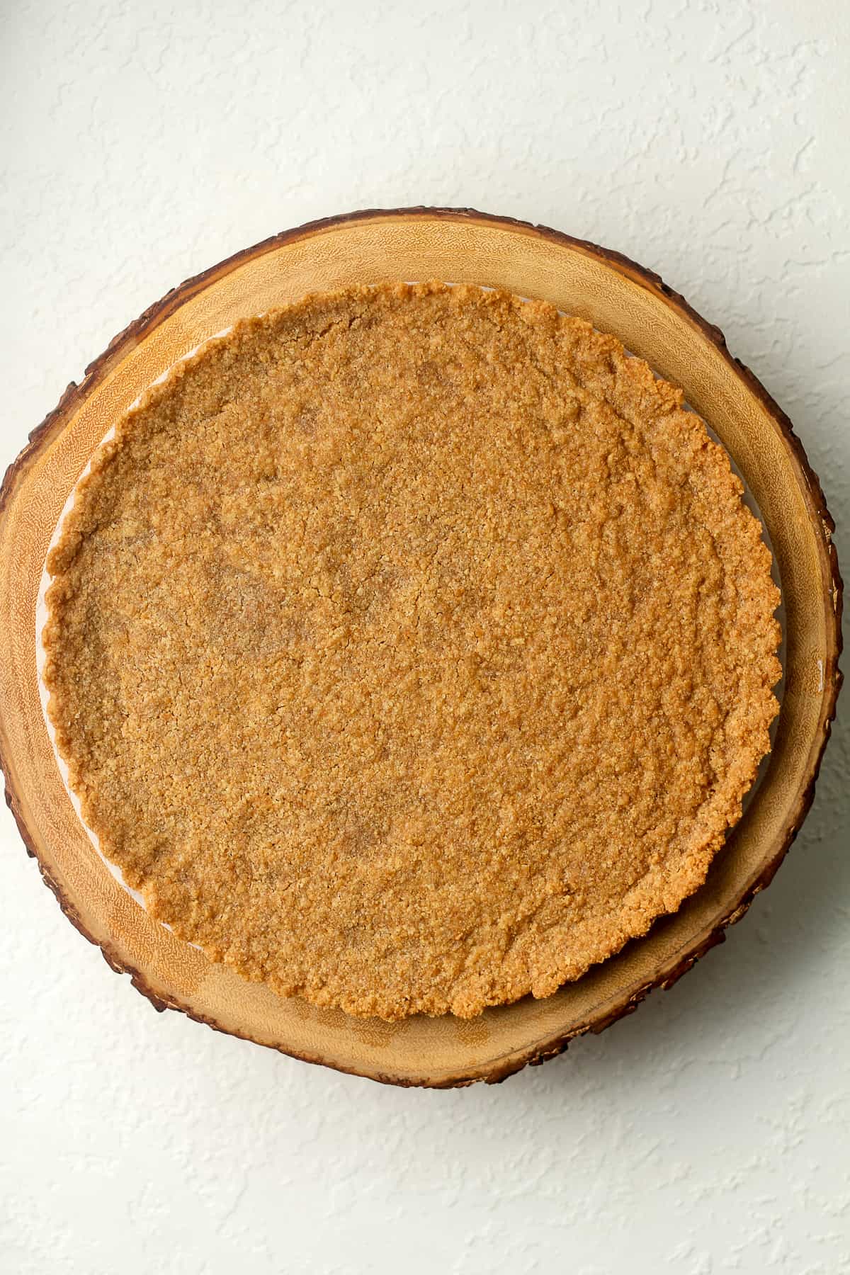 A graham cracker crust on a wooden cake stand.