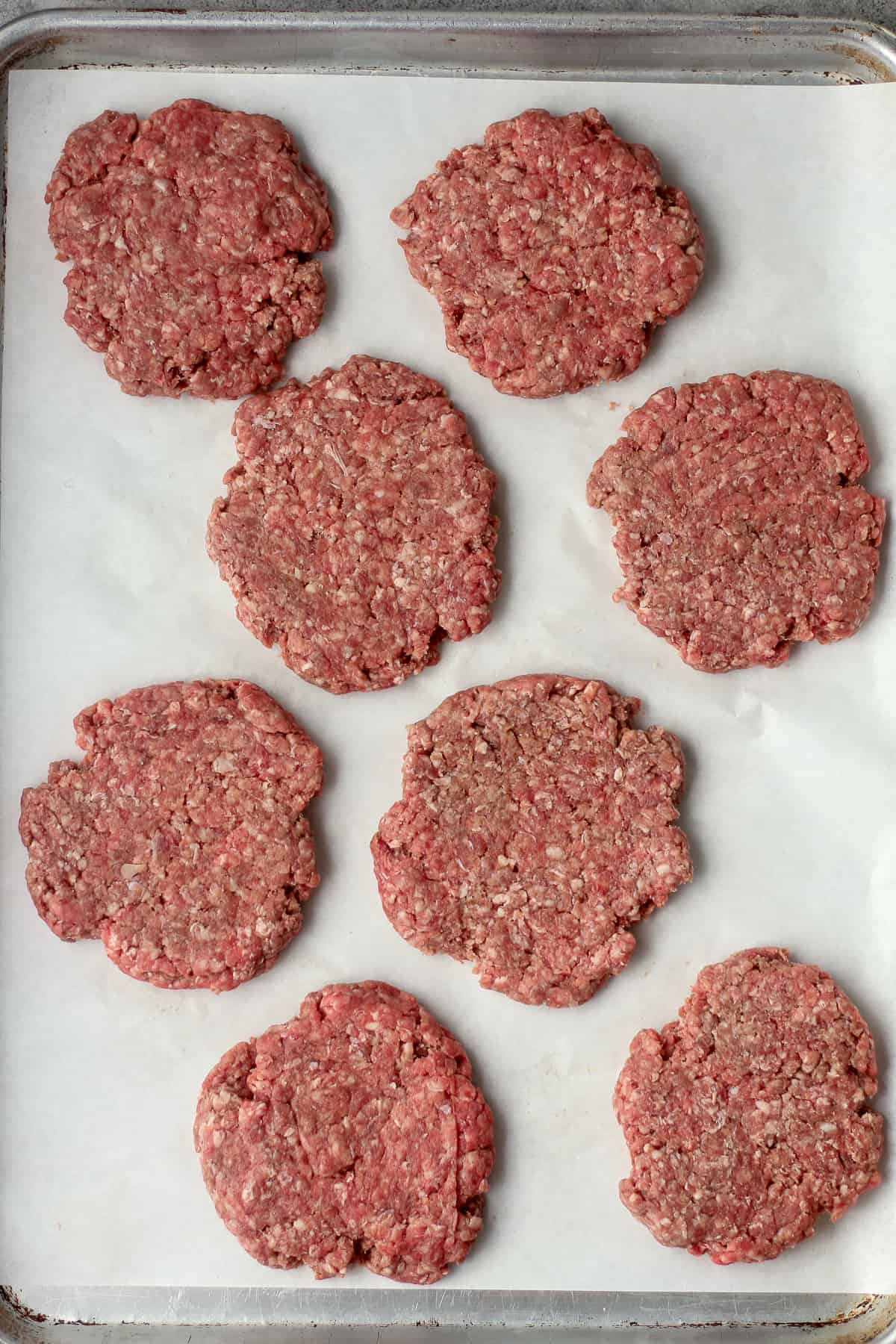 A pan of eight (raw) thin burger patties.