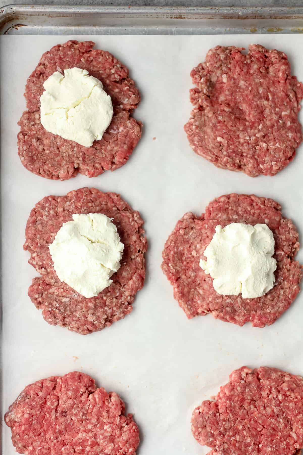 A pan of some thin burger patties with goat cheese in the middle of half of them.