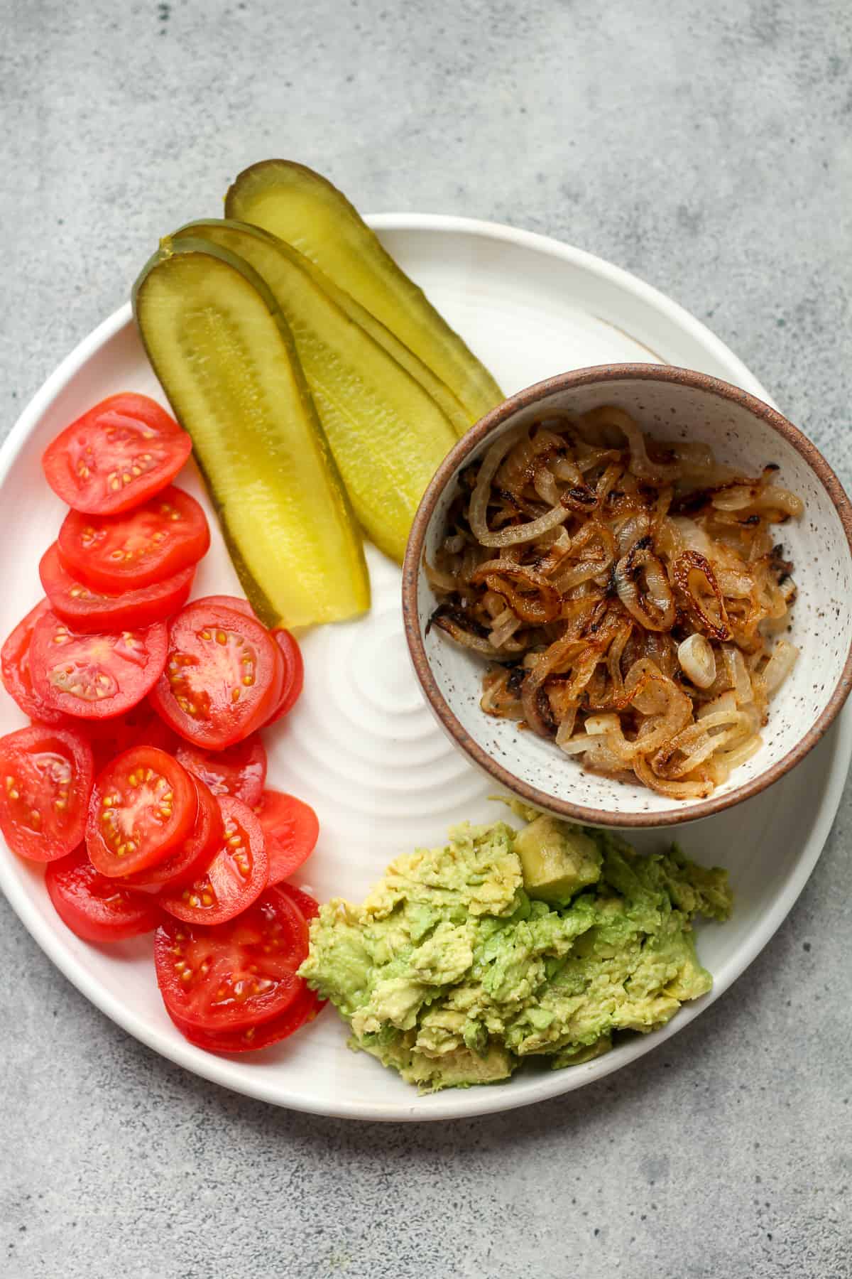 A plate of the toppings - onions, pickles, tomatoes, and avocado.