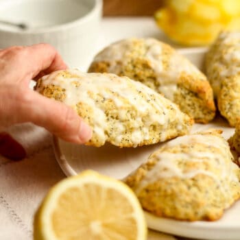 A hand lifting a lemon poppy seed scone off of a plate.