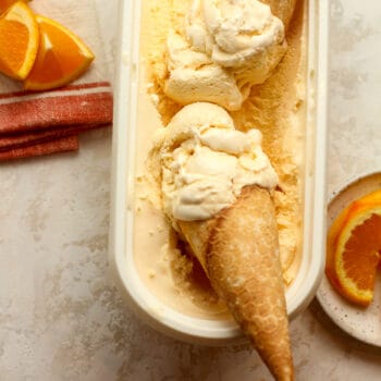 Closeup on some orange ice cream cones in a container of ice cream.