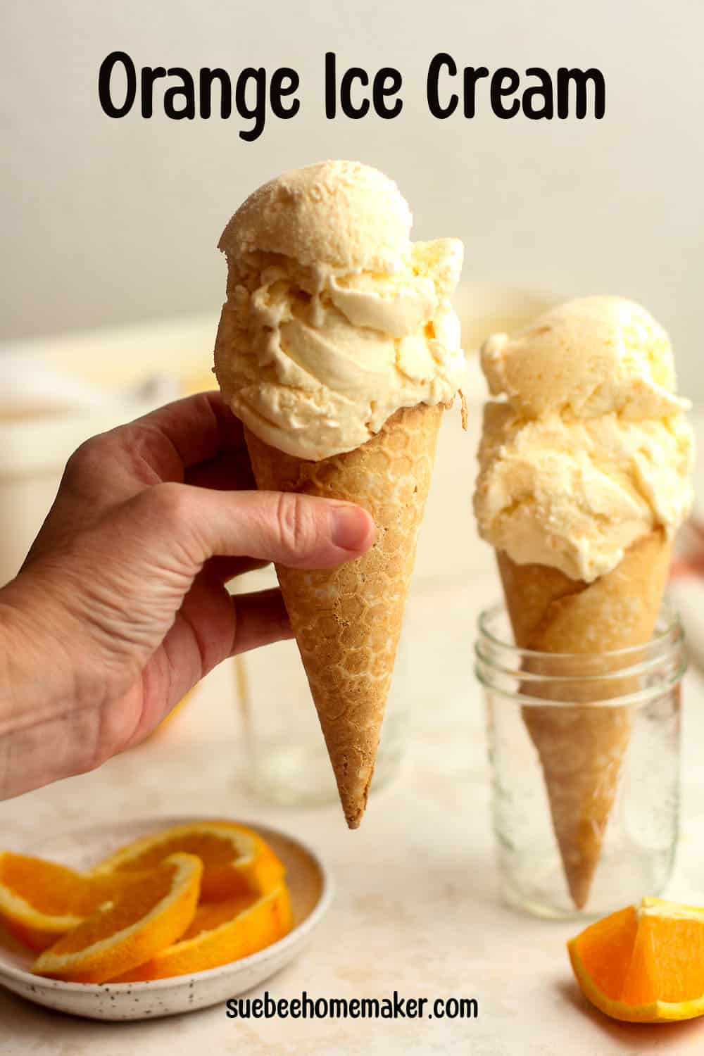 Two cones of orange ice cream, a hand holding one.