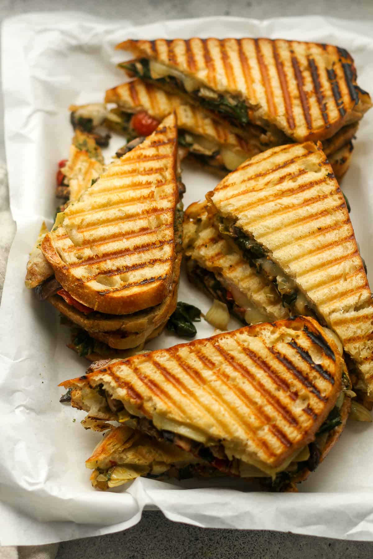 A sheet pan with four halved pesto veggie paninis.