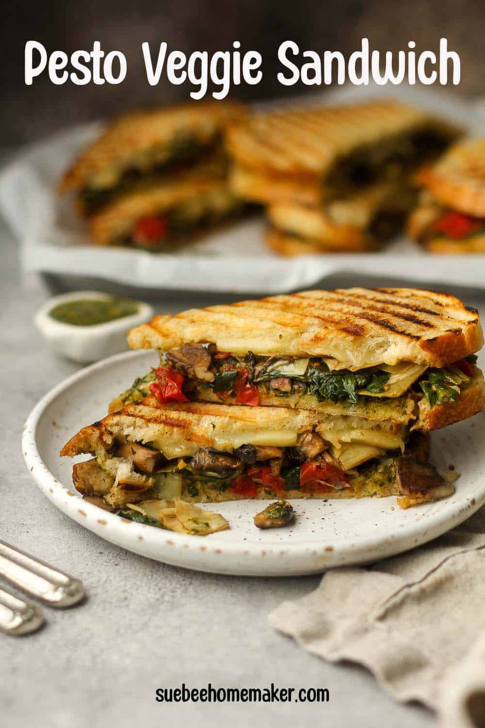 Side view of a plate with a stacked pesto panini with roasted veggies.
