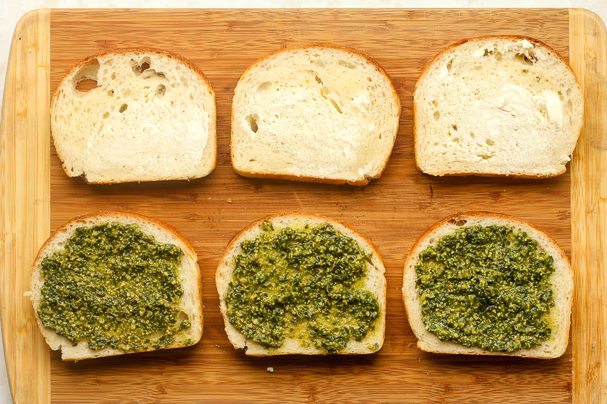 A board with three slices of bread with pesto sauce and three with butter.