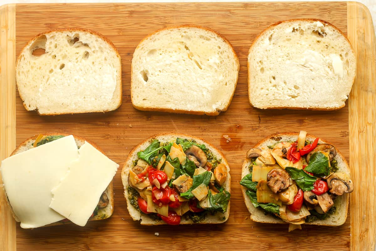 Three open-faced sandwiches being built on a cutting board.