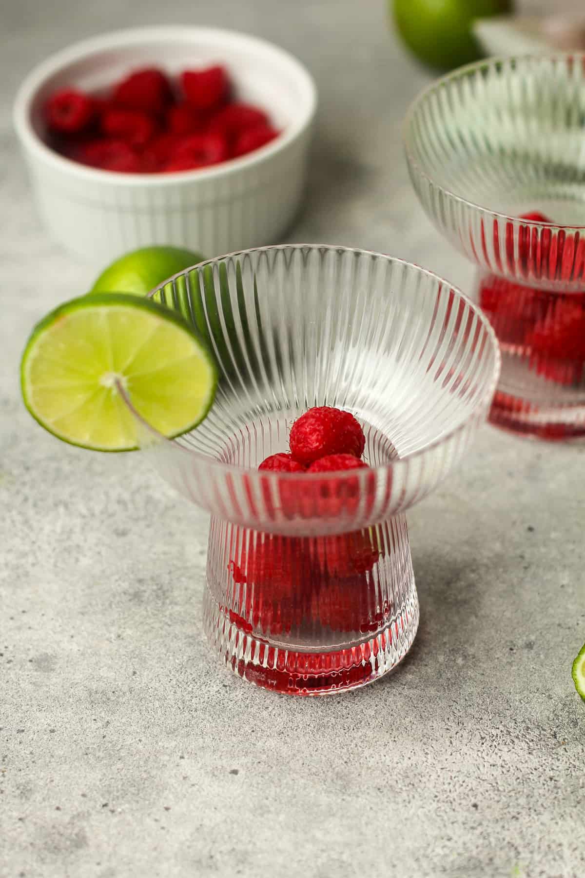 Two prepped glasses with fresh raspberries and lime slices.