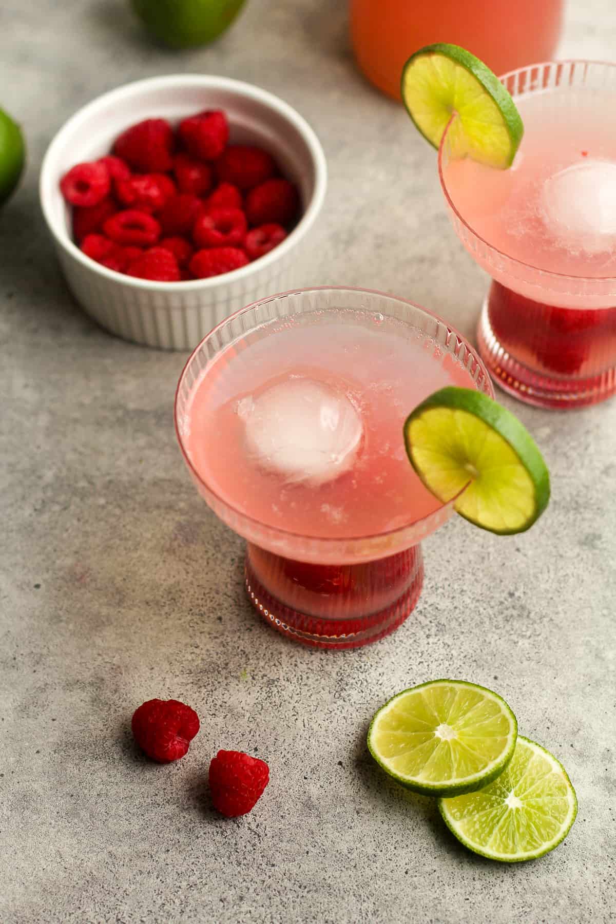 Overhead view of two raspberry drinks with round ice cubes.