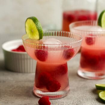 Side view of two glasses of raspberry mocktails with limes.