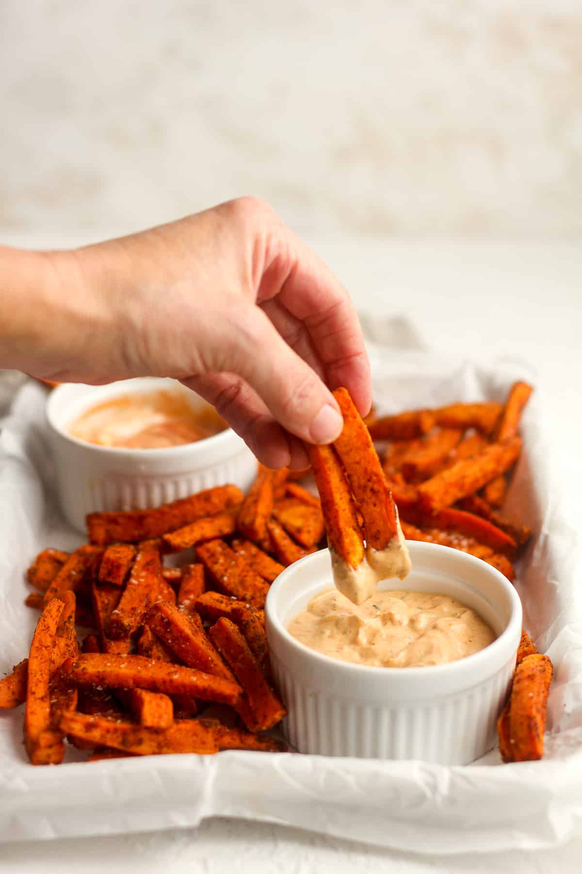 Side view of a tray of sweet potato fries with my hand dipping fries into the sacue.