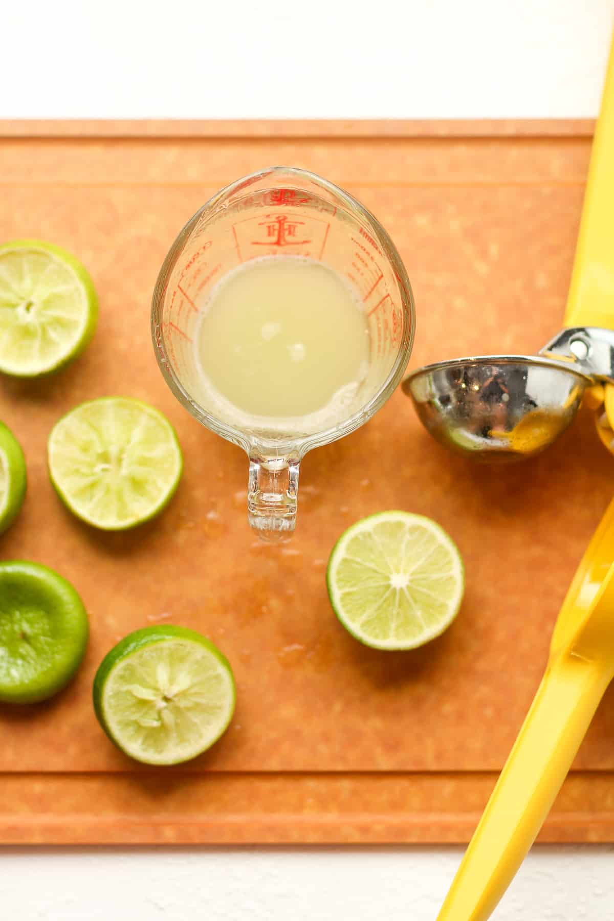 A cutting board with lime halves and a measuring cup of lime juice.