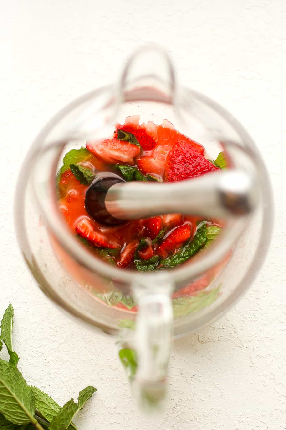Overhead view of a pitcher of strawberries and mint and a muddler.