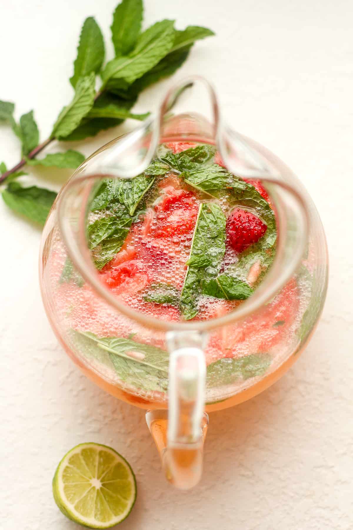 Overhead view of a large pitcher of mojito mocktails with muddled strawberries and mint.