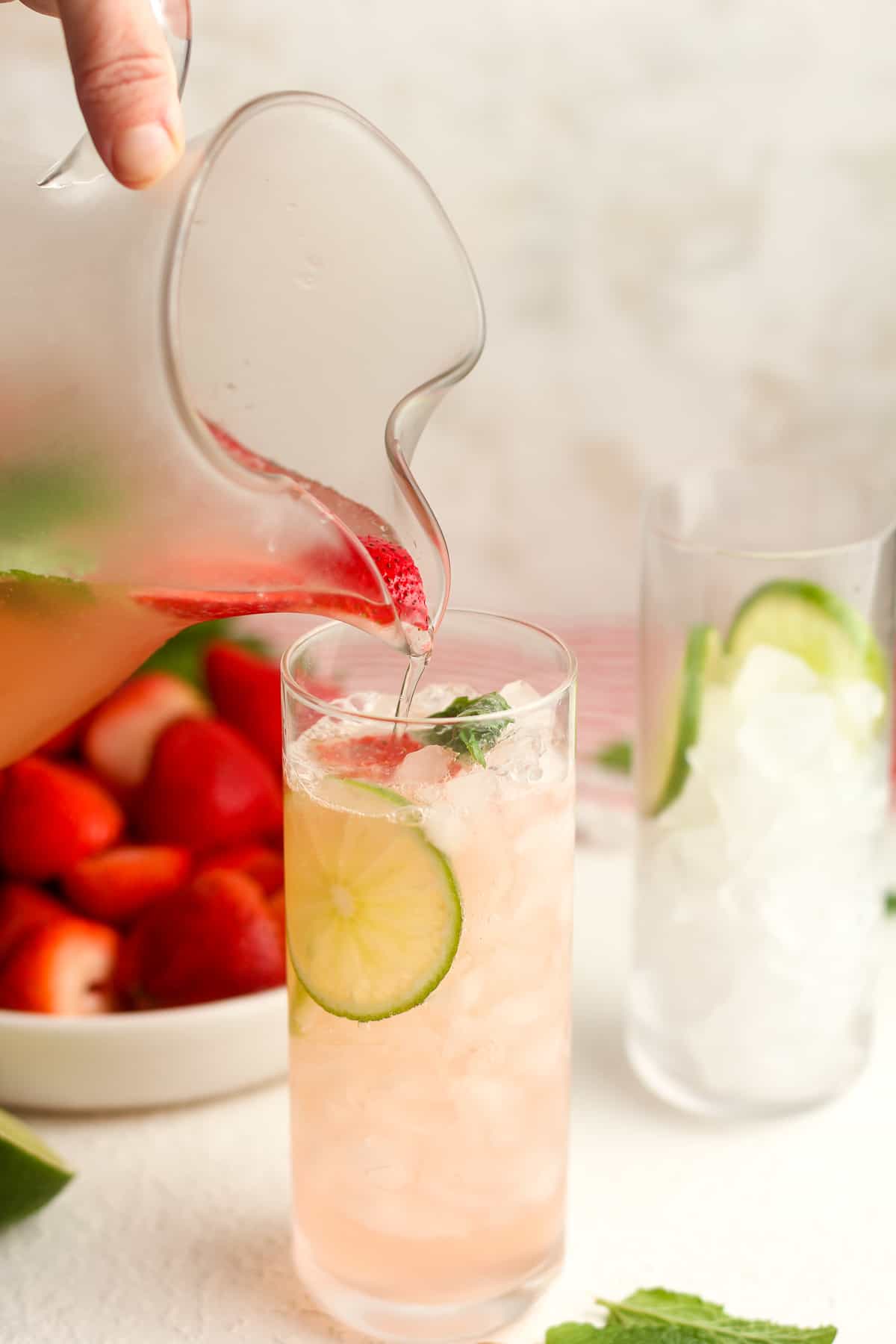 A pitcher of strawberry mojito mocktails being poured into a tall glass.