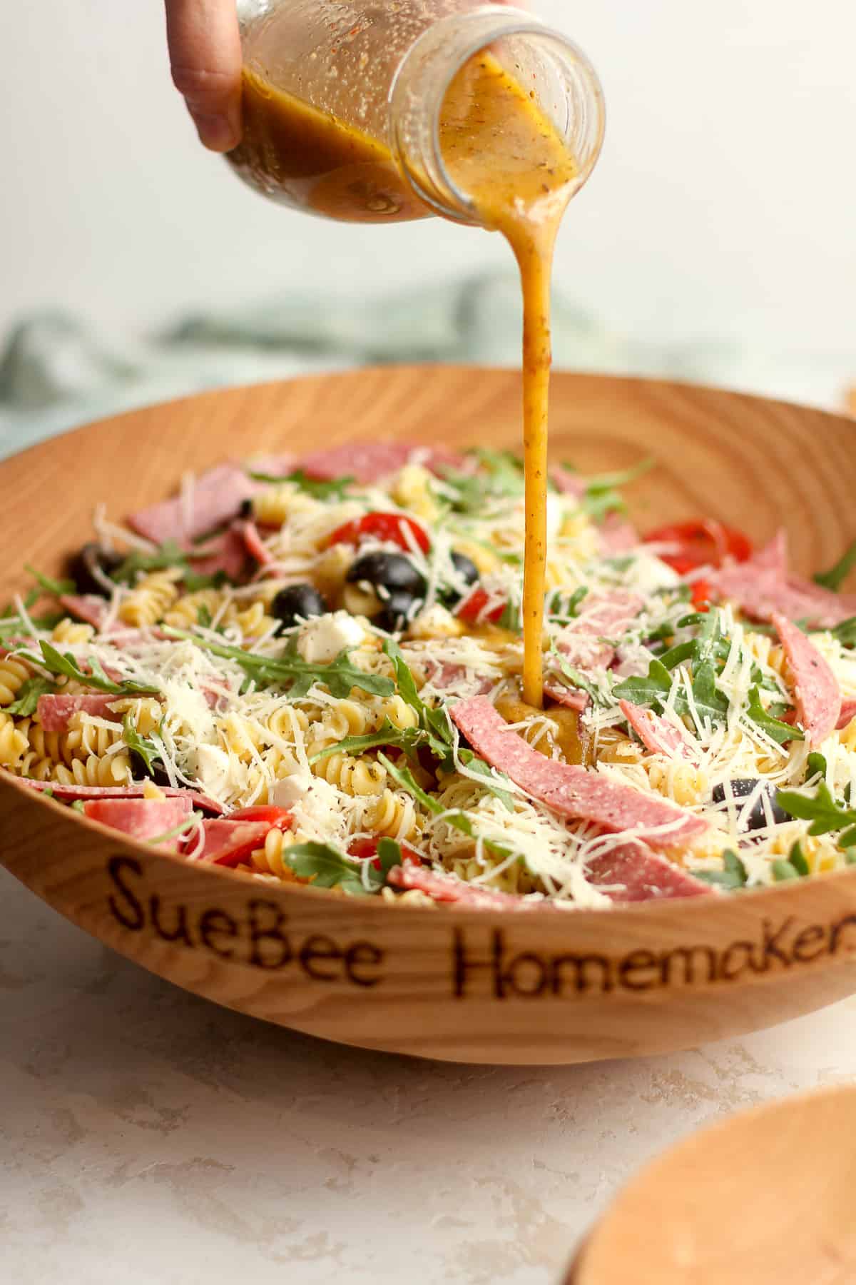Side view of a bowl of the pasta salad with a hand pouring the creamy Italian dressing over the top.
