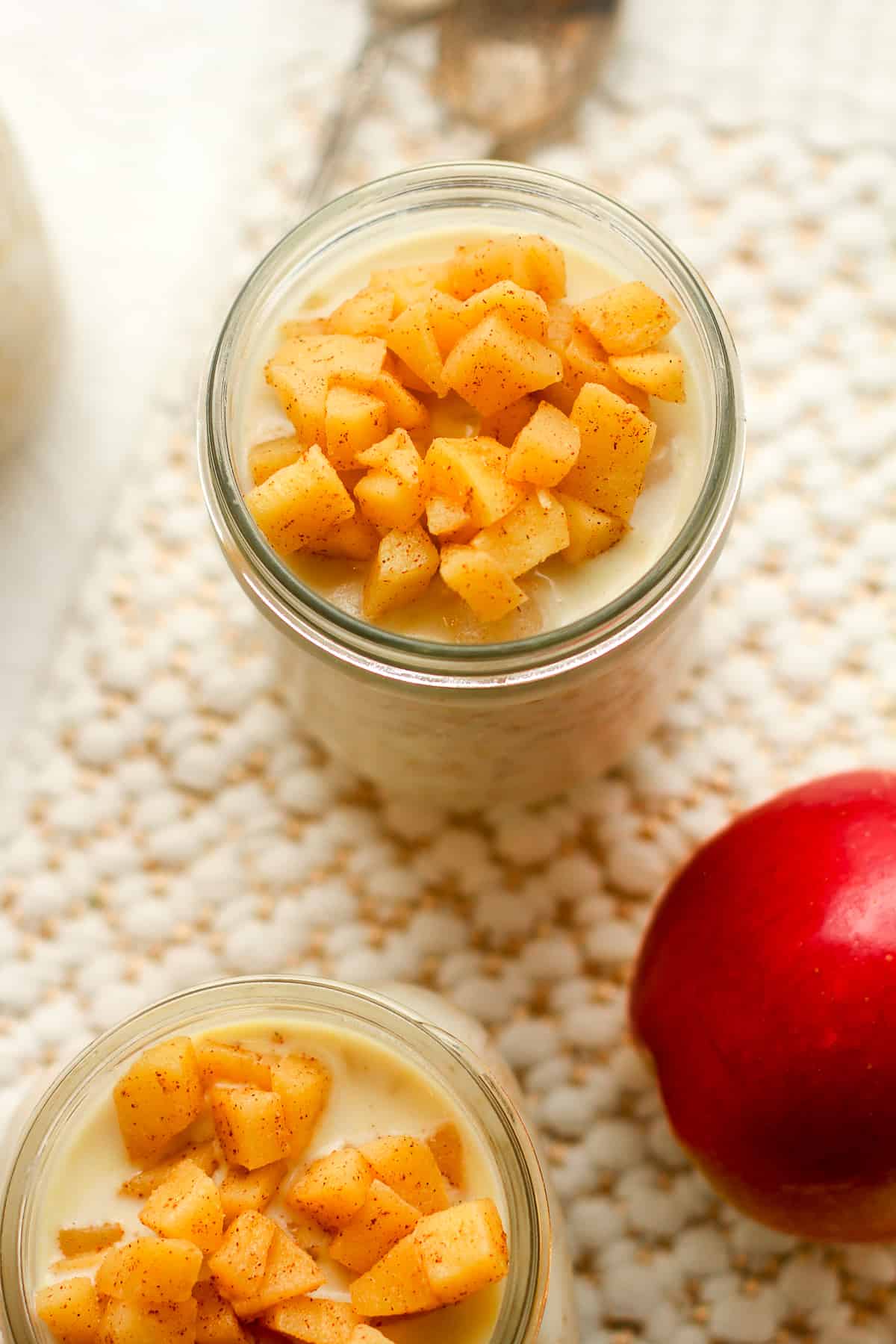 Overhead view of two jars of oats with chunky apples on top.