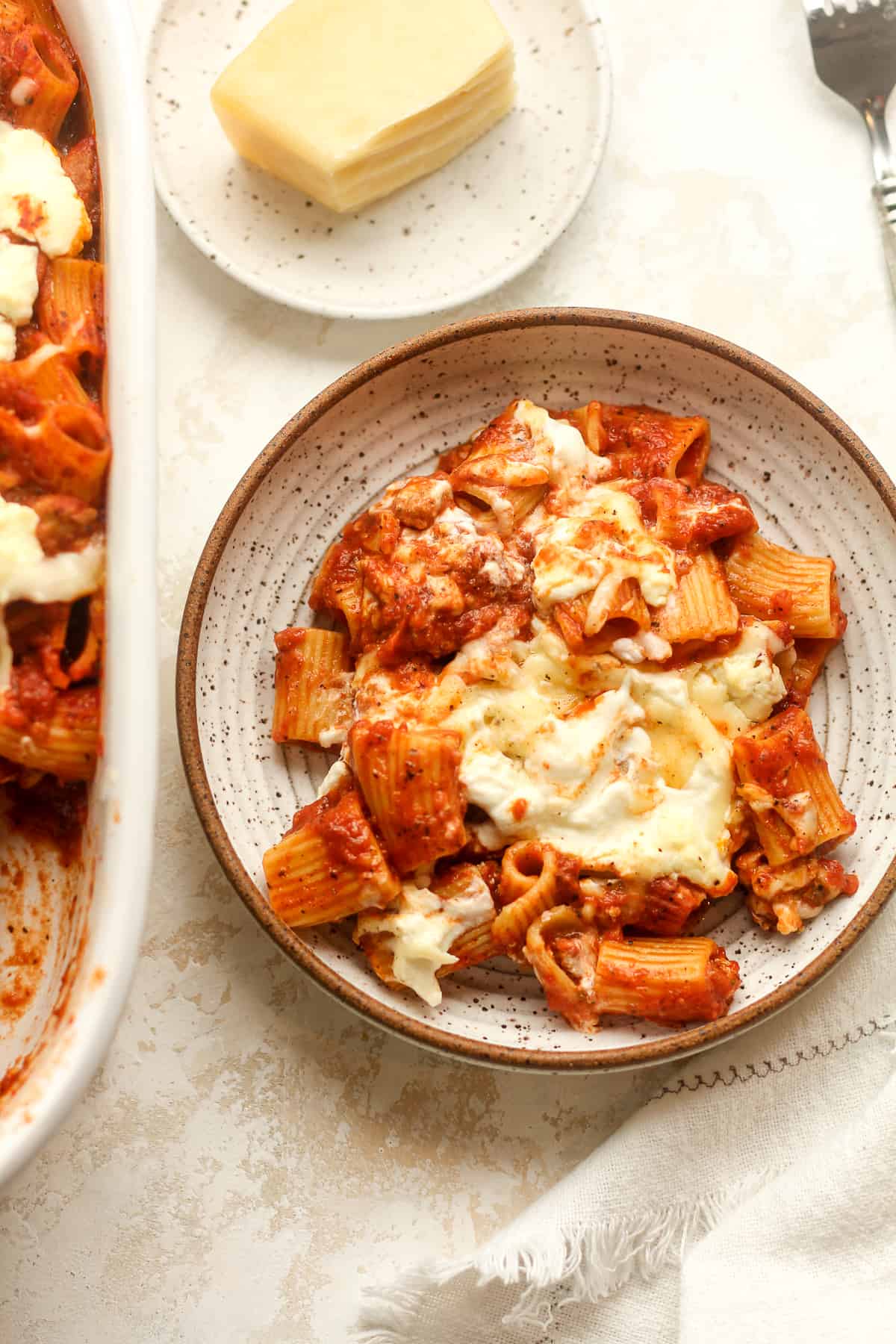 A serving bowl of baked rigatoni pasta next to a casserole dish.