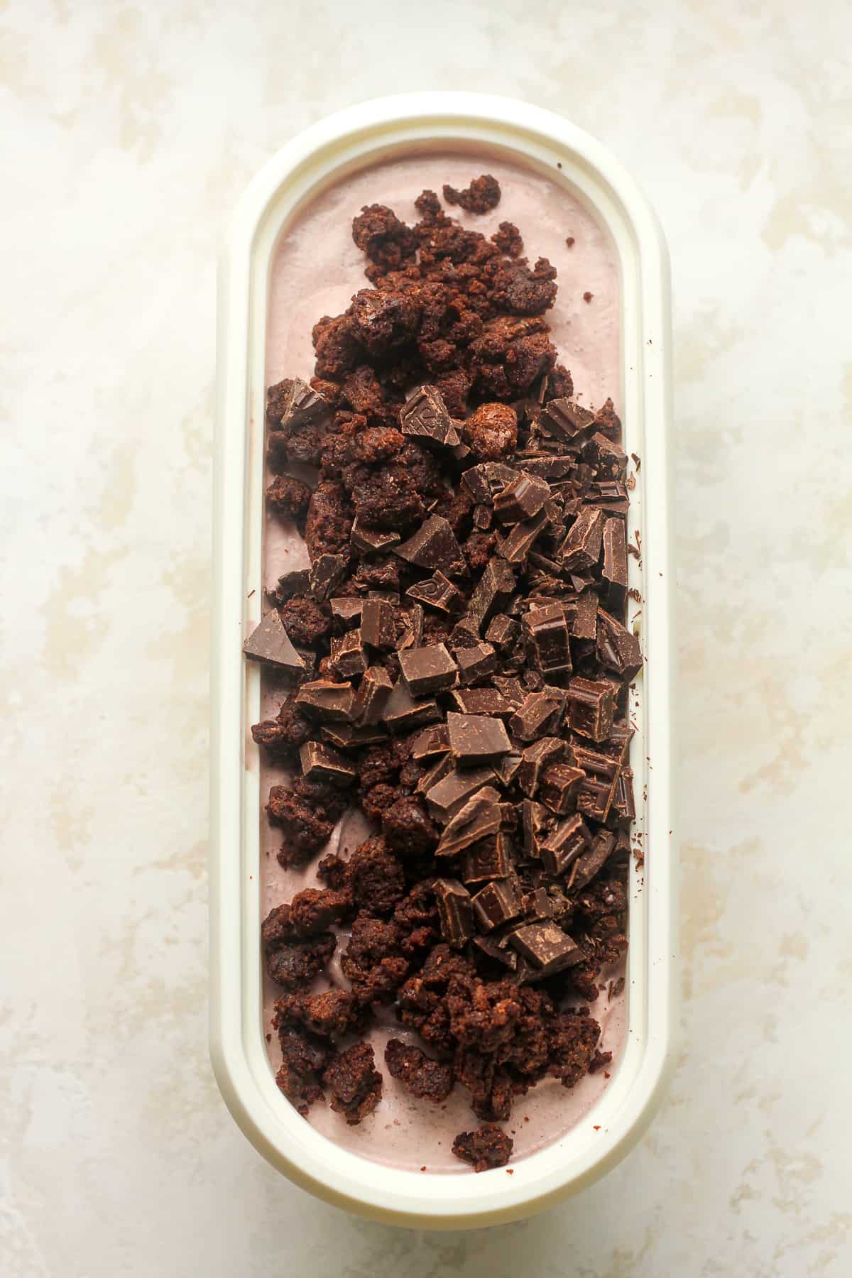 A container with black forest ice cream topped with brownie chunks and chocolate chunks.