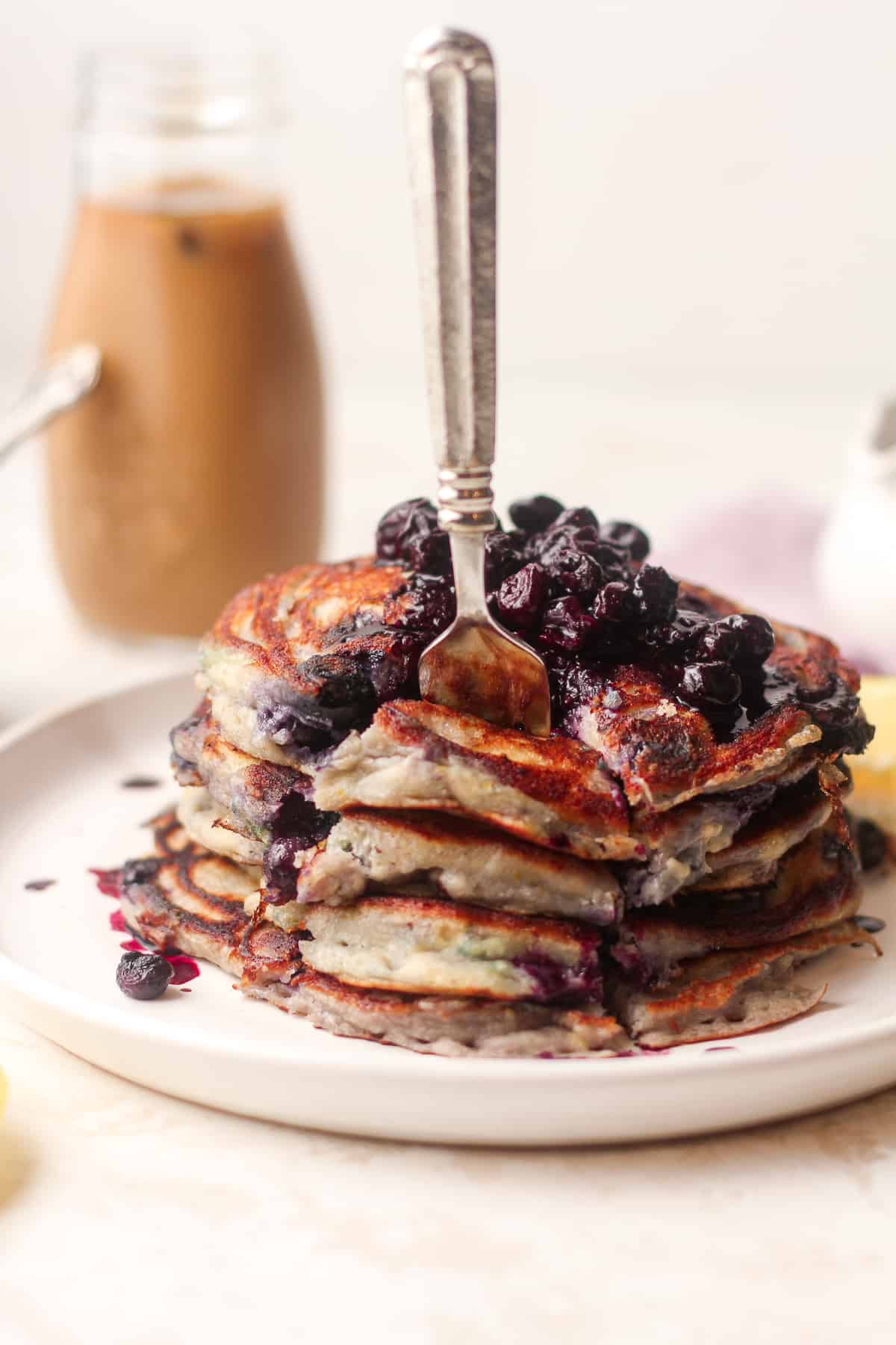 A fork stabbed into a stack of pancakes with blueberry compote on top.