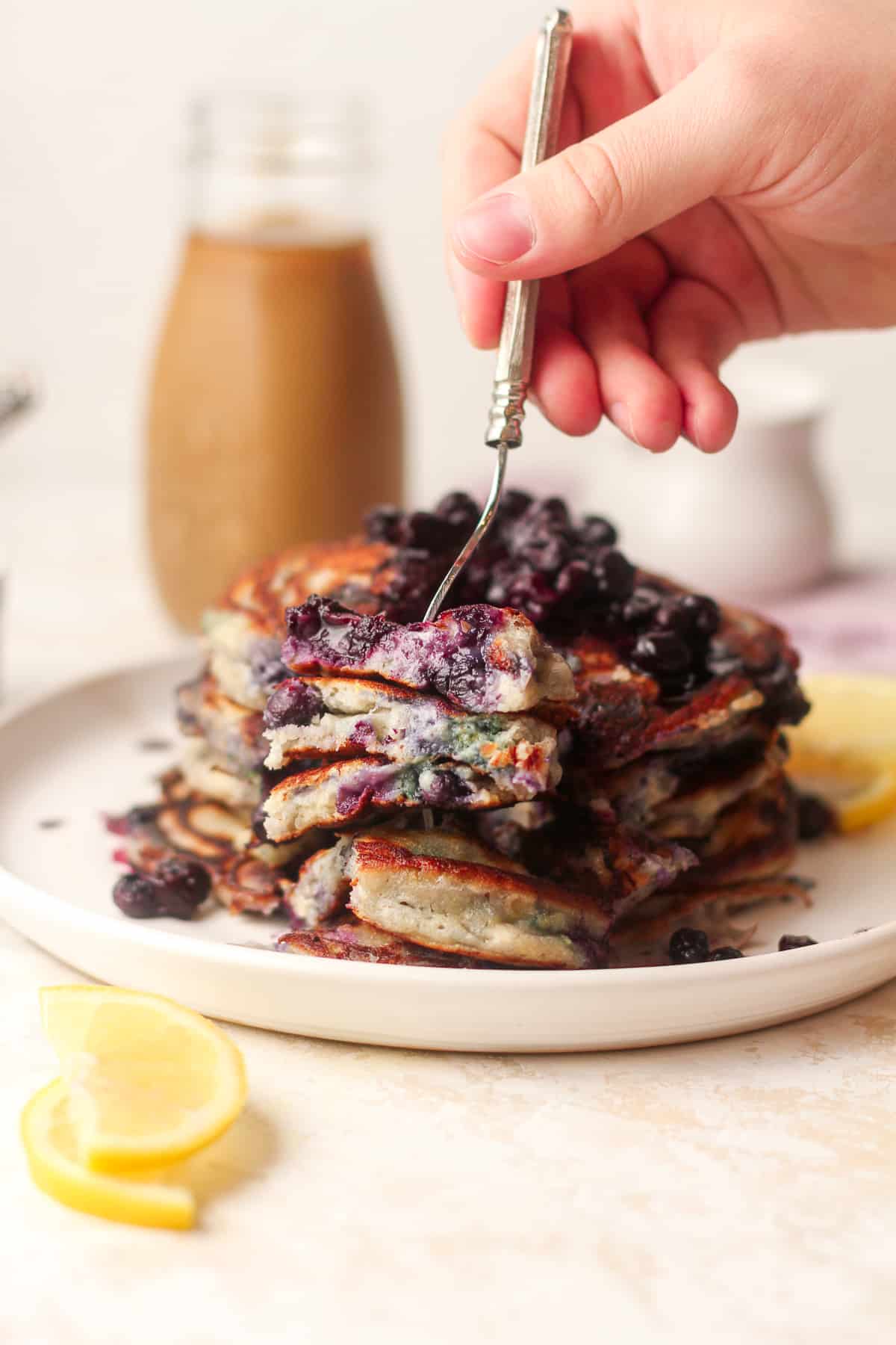 A hand digging a fork into a stack of blueberry pancakes.