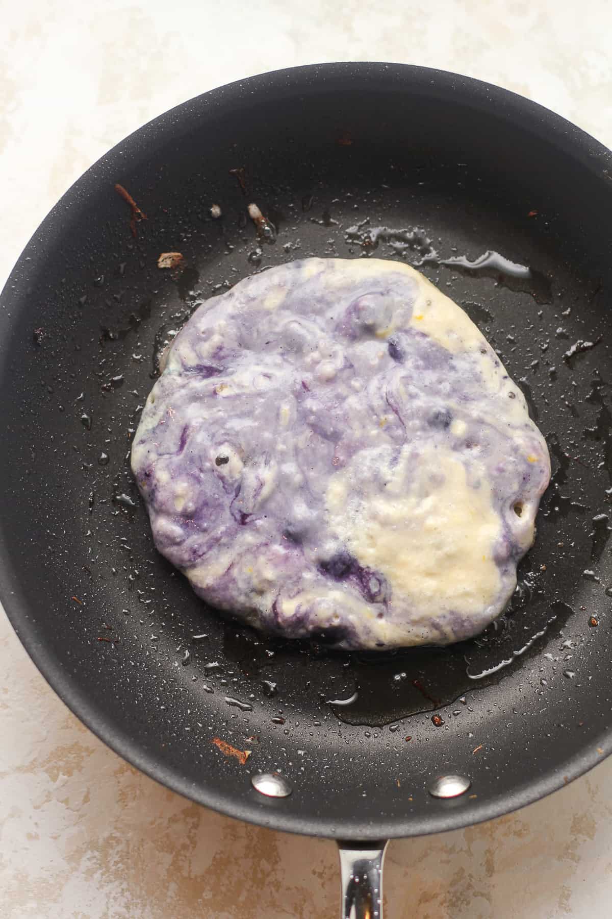 One blueberry lemon pancake in the pan before flipping.
