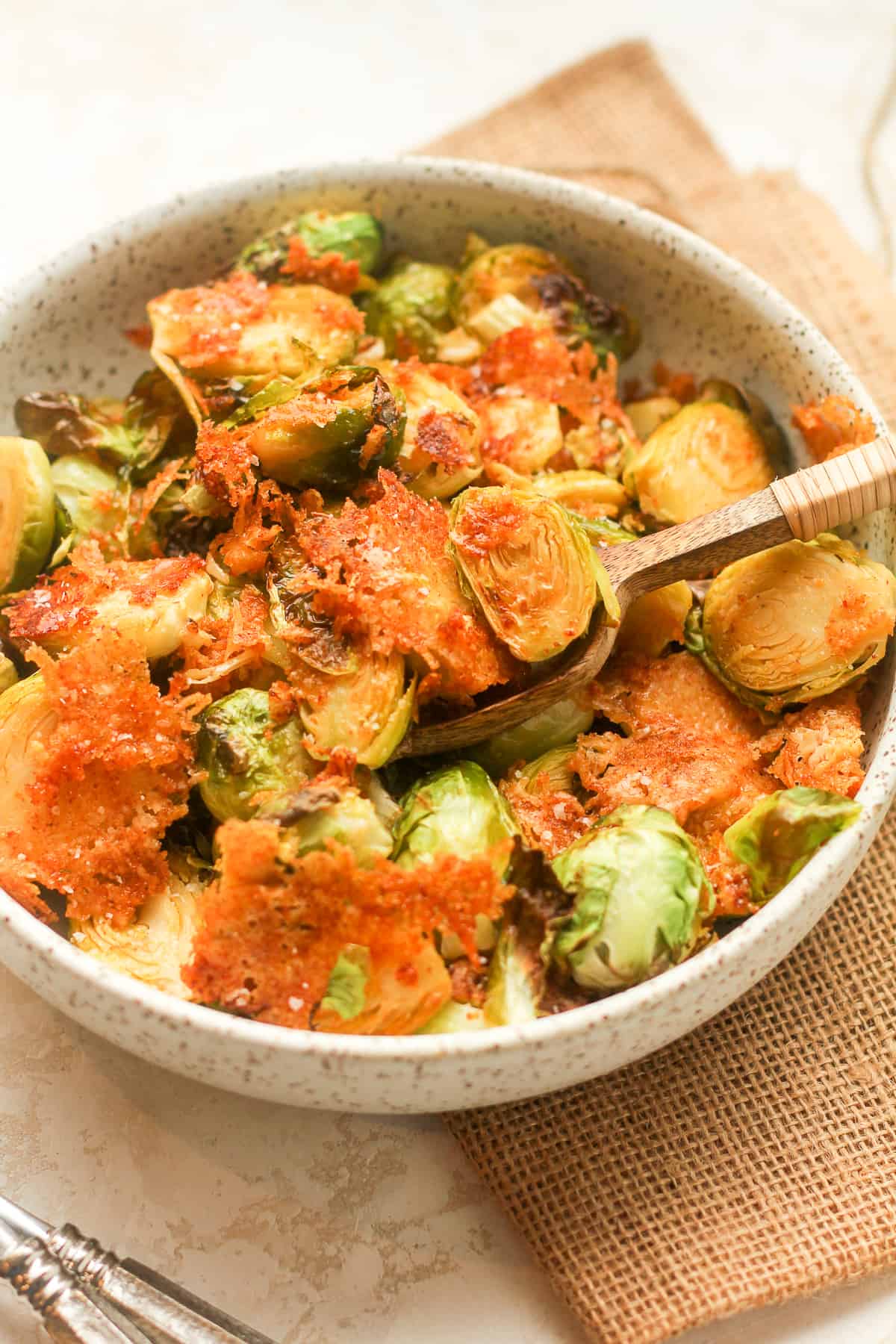 Side view of a bowl of crispy parmesan Brussels sprouts with a wooden spoon.