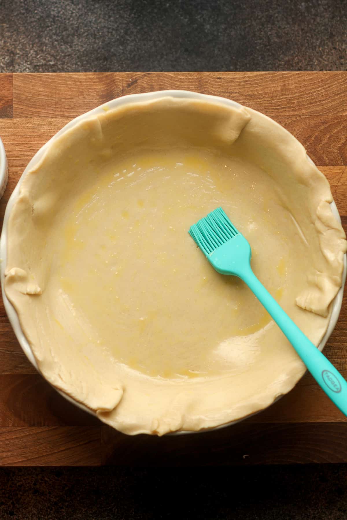 The bottom pie crust on a pie plate with a brush.