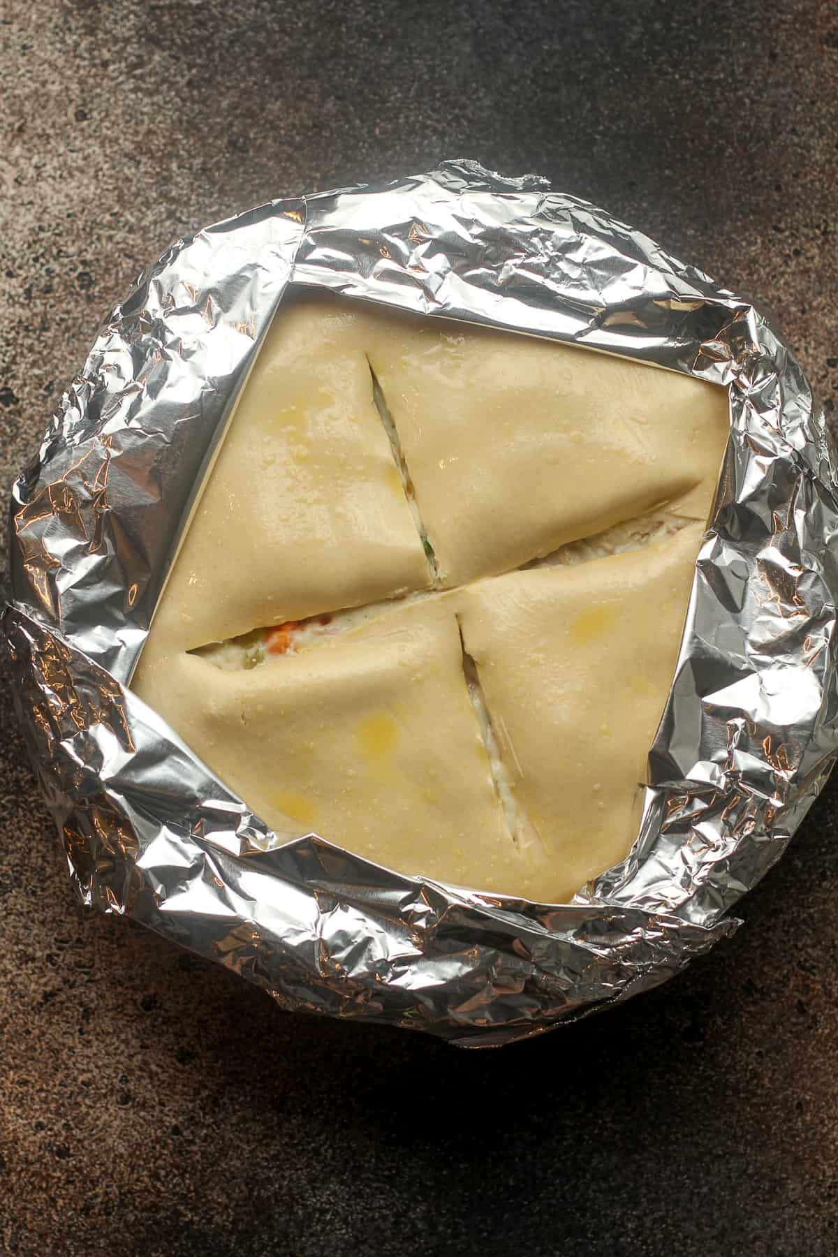 A pot pie with tin foil over the edge3s of the crust.