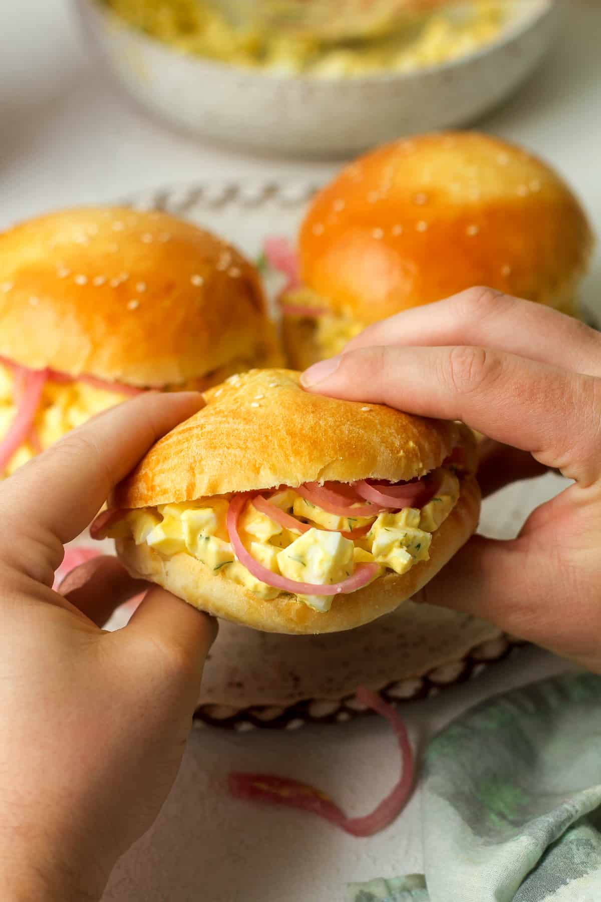 Two hands holding an egg salad sandwich (with red pickled onions).