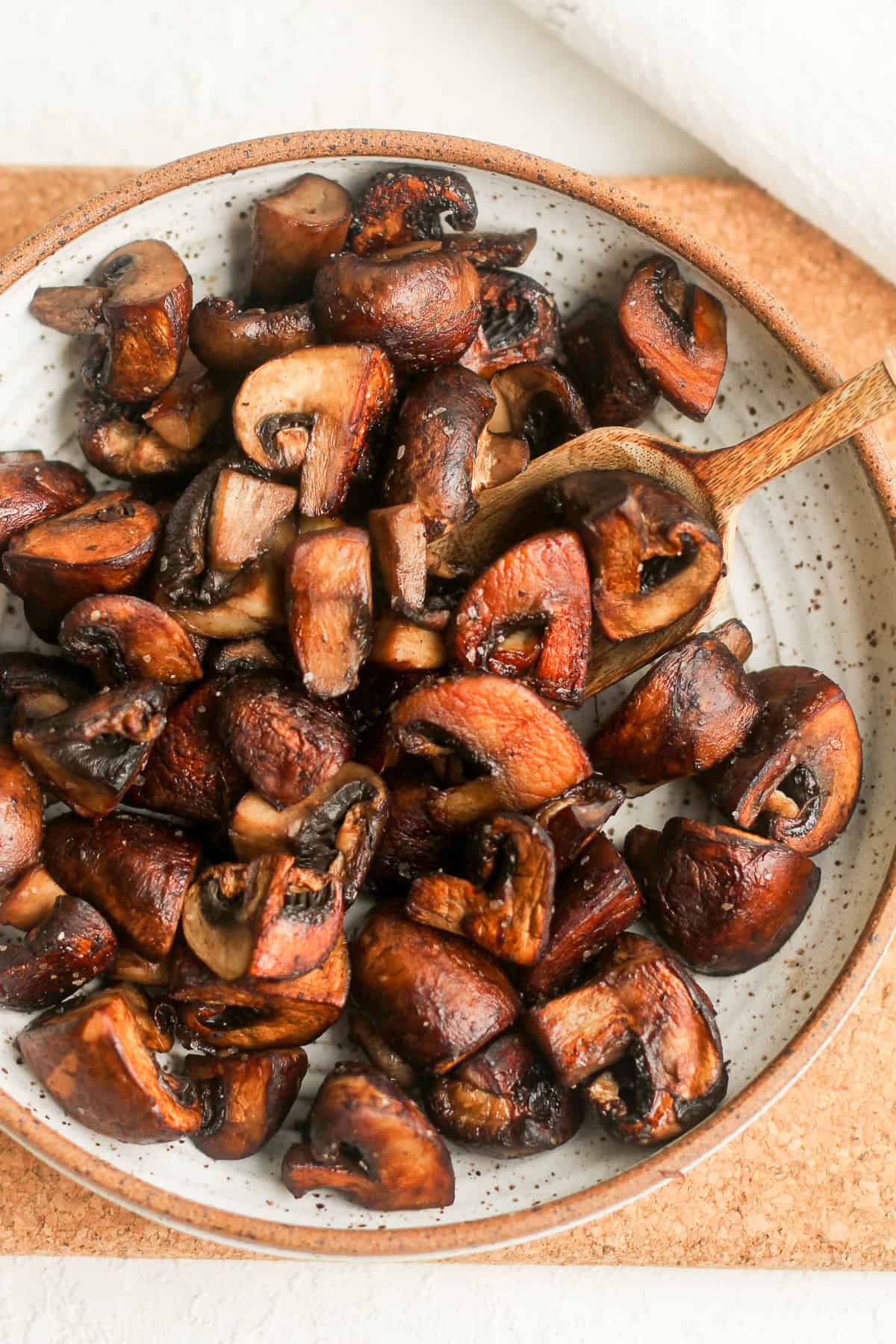 A bowl of browned mushrooms with a spoon.