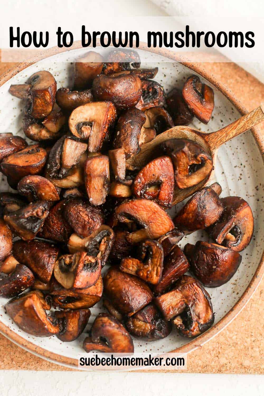 A bowl of browned mushrooms with a wooden spoon.