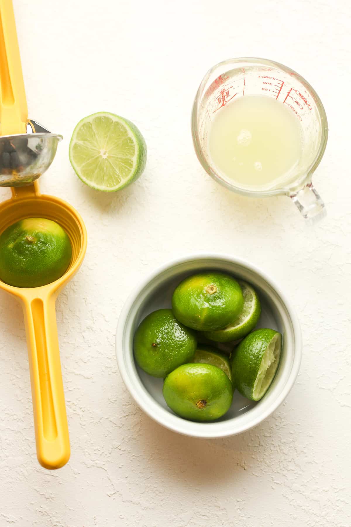 The citrus press with a bowl of lime halves and a measuring cup of lime juice.