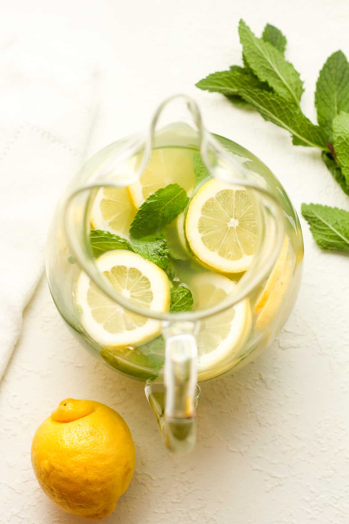 A pitcher of lemon mojitos with lemon and lime slices and mint leaves.