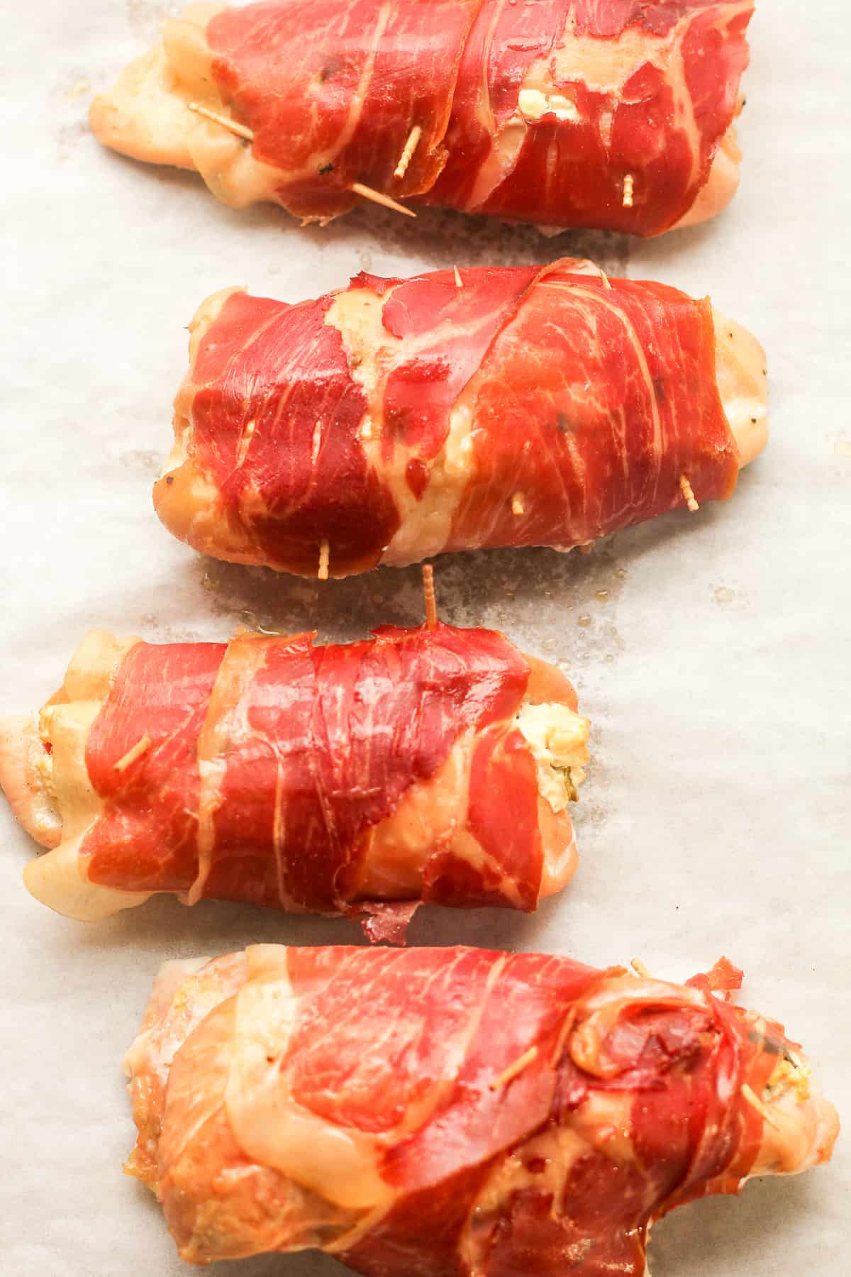 Overhead shot of four chicken breasts stuffed with goat cheese and wrapped in parma ham.