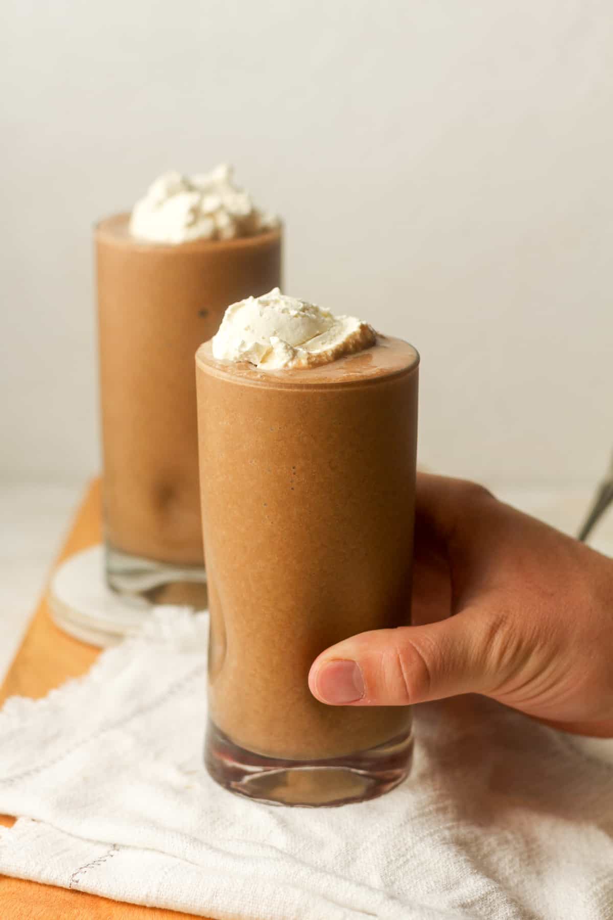 A hand on a tall glass of coffee smoothie with whipped topping.