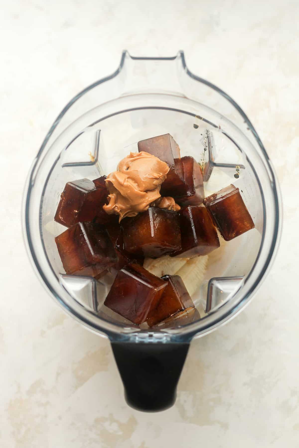 A blender full of the coffee smoothie ingredients, with coffee cubes and peanut butter on top.