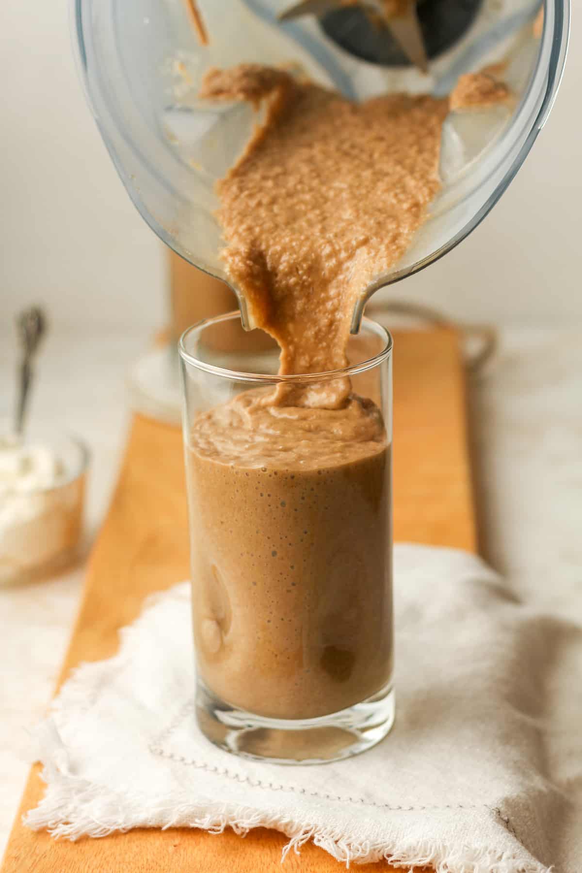 A blender of coffee smoothie pouring into a tall glass.