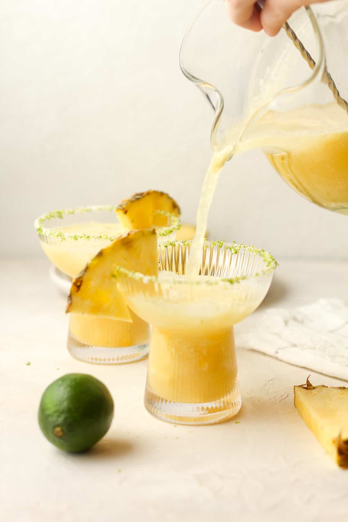 A pitcher of pineapple margaritas pouring into a glass.