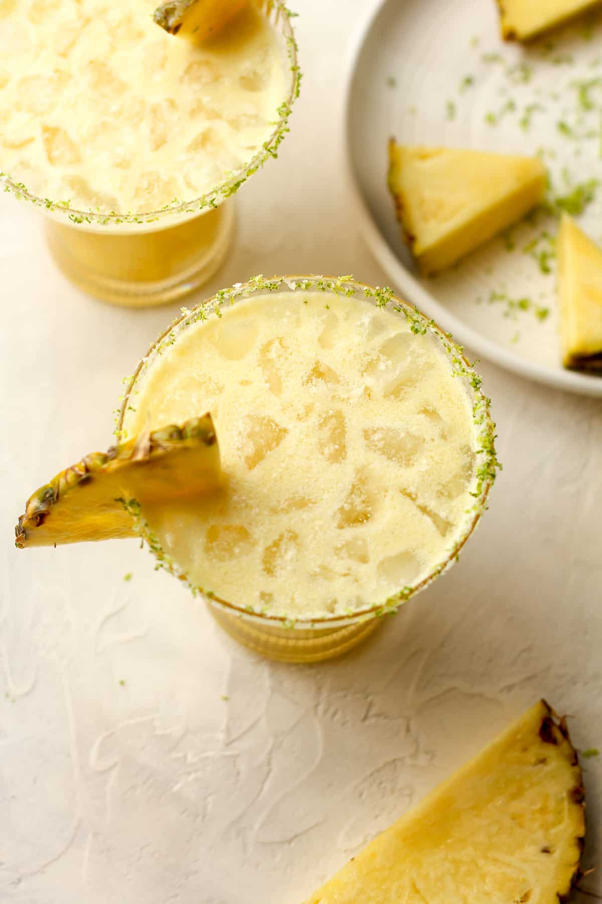 Two glasses of pineapple coconut margaritas with pineapple wedges.